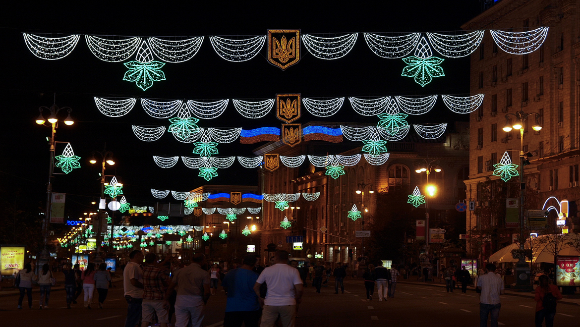 Urban setting with people on the street at night and decorations lit up across the street